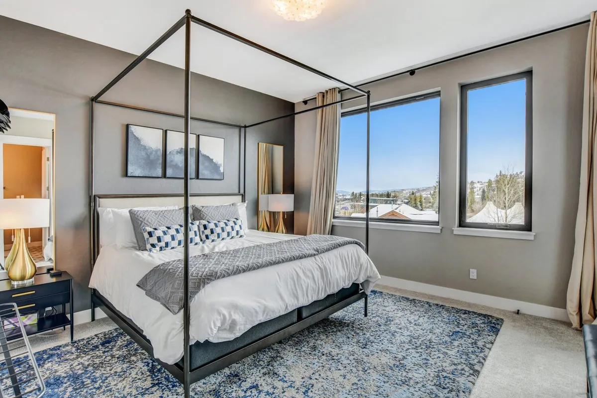 A serene bedroom with a canopy bed, large windows letting in natural light, decorative artwork above the headboard, and a cozy nightstand with a lamp. The design exudes comfort and tranquility, ideal for relaxation after a day of adventure.