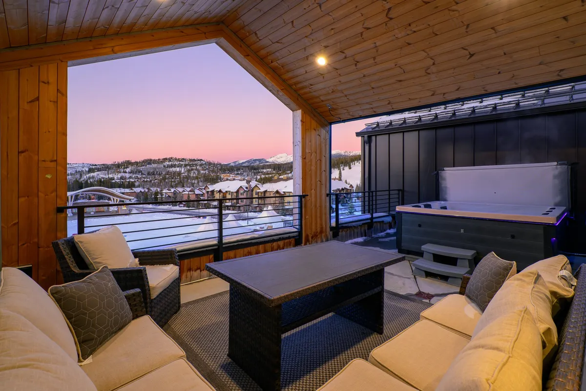 An inviting outdoor scene showcasing a rooftop deck with a hot tub and a comfortable seating area. The space overlooks the mountains, capturing the golden hues of the sunset, and suggests a spot for both relaxation and social gathering. The hot tub and seating area are arranged to maximize the scenic outlook, perfect for enjoying music or events from below.