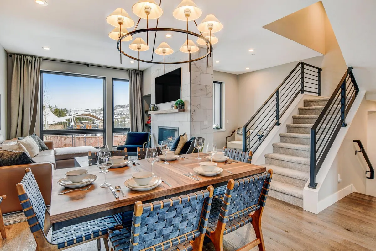 A warm, welcoming open-plan space featuring a dining table with elegant place settings, a glowing chandelier, a cozy fireplace, and a comfortable sofa—all within one seamless environment. The layout supports multiple activities, from family meals to relaxing by the fire or gathering for a movie night.