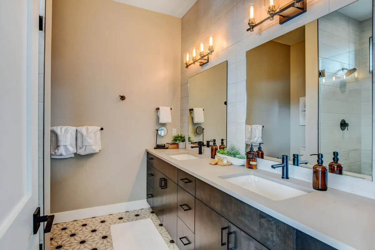 A modern bathroom with a double sink vanity, large mirrors, decorative lighting fixtures, and textured wall tiles. The space is bright and airy, exemplifying a spa-like environment for self-care and relaxation.