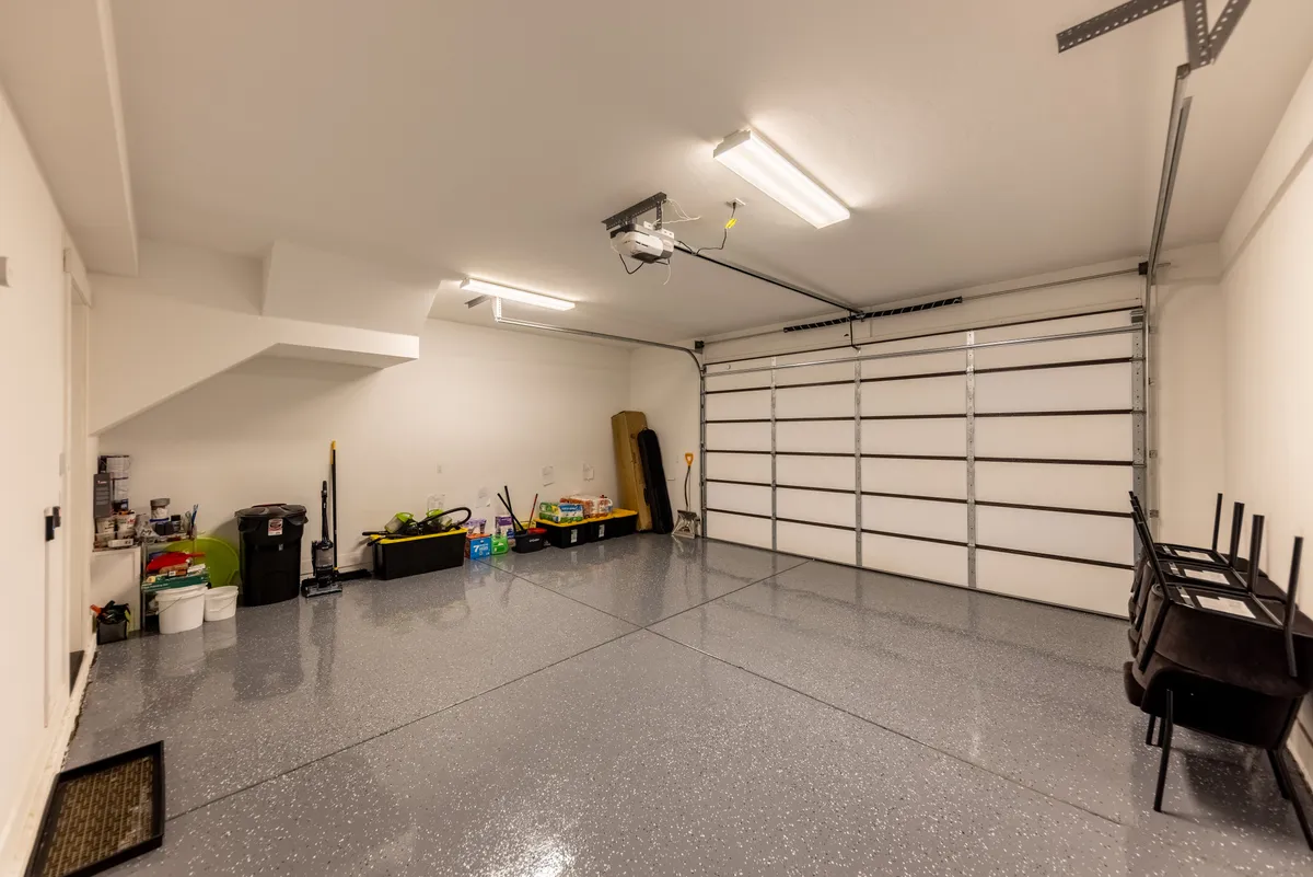 A clean, spacious garage with a modern garage door, spotless flooring, and neatly organized storage bins lining the walls. The scene suggests ample room for storing outdoor recreation equipment, from skis to bikes, as well as easy vehicle access. The uncluttered look highlights the efficiency and practicality of the space.