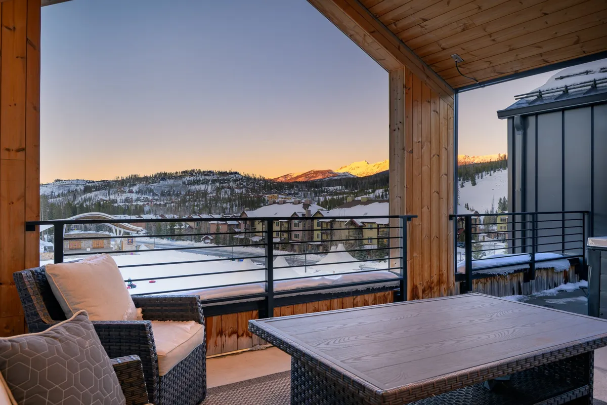 This exterior image showcases a spacious wooden deck with comfortable outdoor seating, offering sweeping views of the surrounding mountains. The architecture features warm wood tones and large openings, emphasizing a seamless connection to the outdoors. The tranquil setting is ideal for relaxing, socializing, or stargazing.